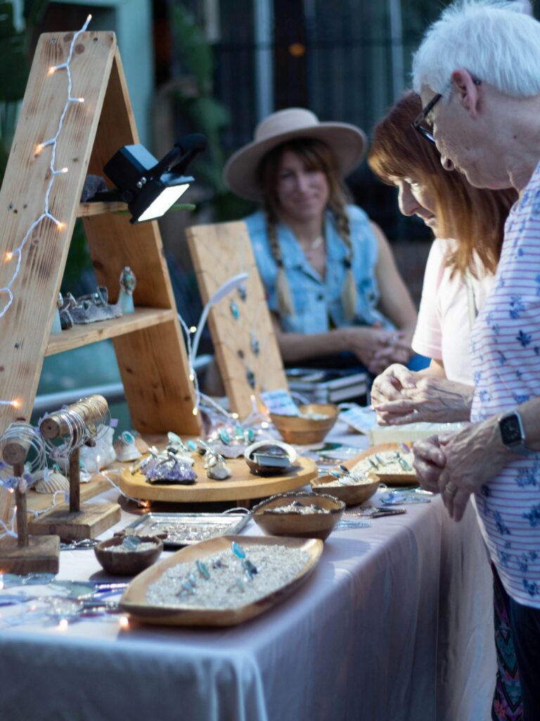 pexels-photo-3617724-3617724 Shoppers browse handcrafted jewelry at an outdoor artisan market stall.